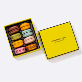 Box of colorful macarons with a yellow lid beside it