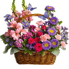 Mixed pink and purple flowers in a wicker basket with butterfly picks
