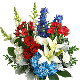 Bouquet of red roses, white lilies, blue hydrangeas, and red alstroemeria in a glass vase