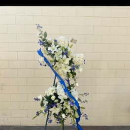 Standing floral spray with white lilies and blue flowers on an easel