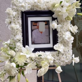White floral funeral frame with lilies and chrysanthemums around a portrait