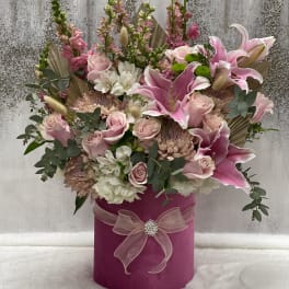 Pink and white floral arrangement in a magenta hat box with a ribbon bow