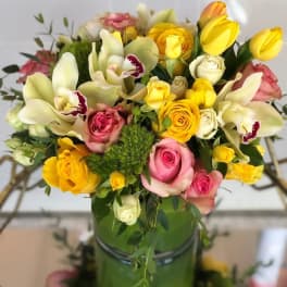 Bouquet of yellow and pink roses with white orchids in a green vase