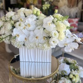 White floral arrangement in a tall ribbed vase with orchids and roses