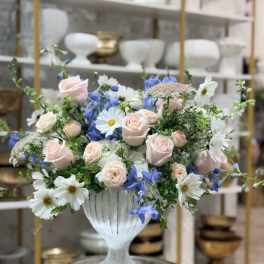 Pastel bouquet of pink roses, white daisies, and blue flowers in a white vase