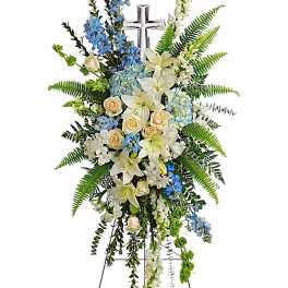 Standing floral spray with white lilies, cream roses, and blue flowers on an easel