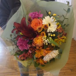 Mixed bouquet with orange, burgundy, white, and pink flowers wrapped in green paper