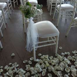 White chair with a small floral bouquet and tulle, surrounded by scattered petals