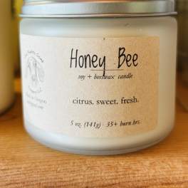 A frosted jar candle with a silver lid and Honey Bee label