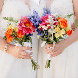 Bride holding two colorful bouquets with pink, orange, blue, and yellow flowers
