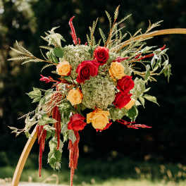 Red and yellow roses arranged with greenery on a gold arch