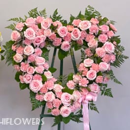 Heart-shaped pink rose and carnation wreath on a stand with a ribbon