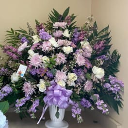 Large lavender and white floral arrangement in a white urn with a purple bow