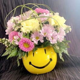 Pink and yellow daisy bouquet in a yellow smiley-face container