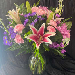 Bouquet of pink lilies, carnations, and purple daisies in a glass vase