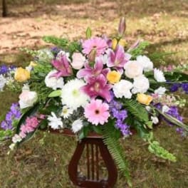 Large mixed flower arrangement with pink lilies, roses, and daisies on a stand