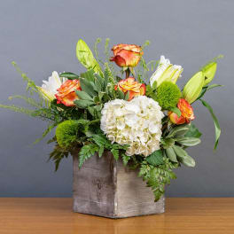 Bouquet of orange roses, white hydrangea, and lilies in a wooden box