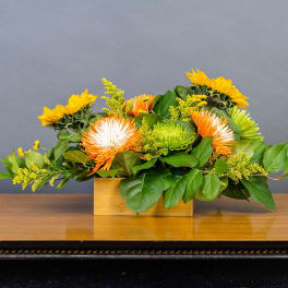Low floral arrangement with sunflowers and orange-white blooms in a wooden box