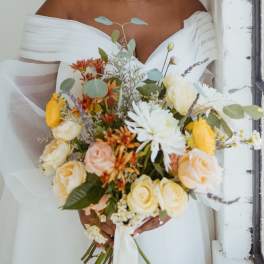 Bride holding a bouquet of cream, yellow, and orange flowers