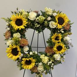 Heart-shaped floral wreath with sunflowers, white roses, and cream blooms on a stand