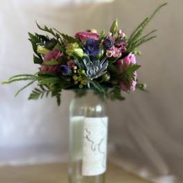 Colorful mixed bouquet with pink and blue flowers arranged in a tall glass bottle.