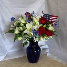 Bouquet of red roses, white lilies, and blue flowers in a dark vase with an American flag