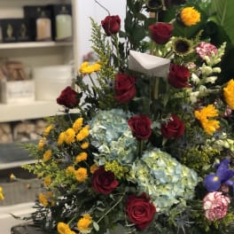 Tall floral arrangement with red roses, blue hydrangeas, and yellow blooms