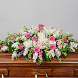 Pink and white casket spray with roses, lilies, and hydrangeas on a wooden casket