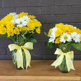 Two yellow and white daisy bouquets in glass vases with ribbon bows