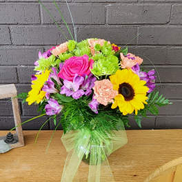 Mixed bouquet with pink roses, sunflowers, and purple flowers in a glass vase