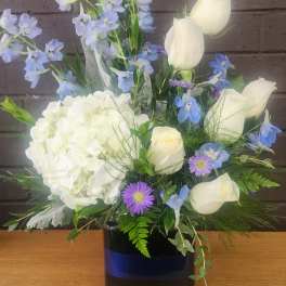 White roses and hydrangea with blue flowers in a dark vase