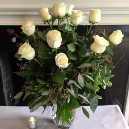 Cream roses arranged in a clear glass vase with greenery.
