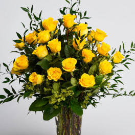 Yellow roses arranged in a clear glass vase with greenery