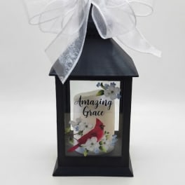 Black lantern with a white bow and a candle labeled Amazing Grace
