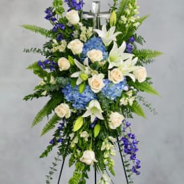 Standing floral spray with white lilies, cream roses, blue hydrangeas, and purple flowers