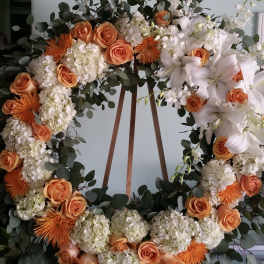 Large floral wreath with orange roses, white lilies, and white hydrangeas