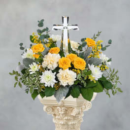 Yellow and white floral arrangement with a clear cross centerpiece in a decorative vase