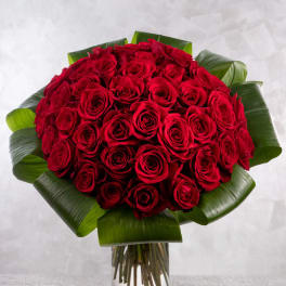 Bouquet of red roses with broad green leaves in a clear glass vase