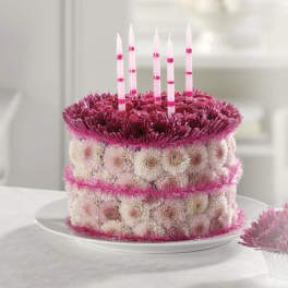 Round pink and white floral cake arrangement with striped pink candles on a white plate