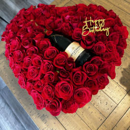 Heart-shaped rose arrangement with a champagne bottle and birthday topper