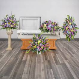 Set of pastel funeral flower arrangements surrounding an open casket in a chapel.