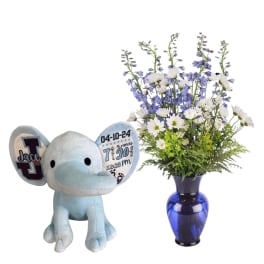 Blue plush elephant beside a blue vase of white and purple flowers