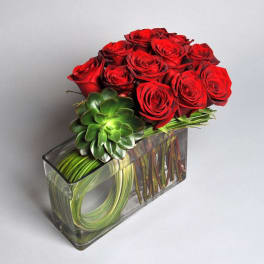 Red roses arranged in a clear rectangular vase with a green succulent accent