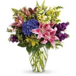 Mixed bouquet of pink lilies, blue hydrangea, and purple flowers in a glass vase