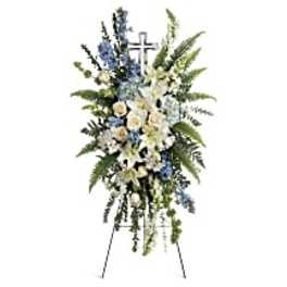 Standing funeral spray with white lilies, roses, and blue flowers on an easel