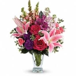 Bouquet of pink lilies, red roses, and purple flowers in a clear vase