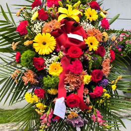 Large standing floral spray with red roses and yellow lilies on a red ribboned easel