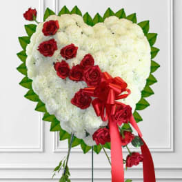 Heart-shaped white floral arrangement with red roses and a red ribbon