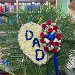 Heart-shaped floral tribute with white flowers, red roses, and blue letters