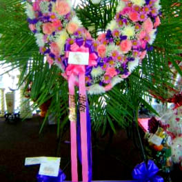 Heart-shaped floral wreath with pink, white, and purple flowers on a stand
